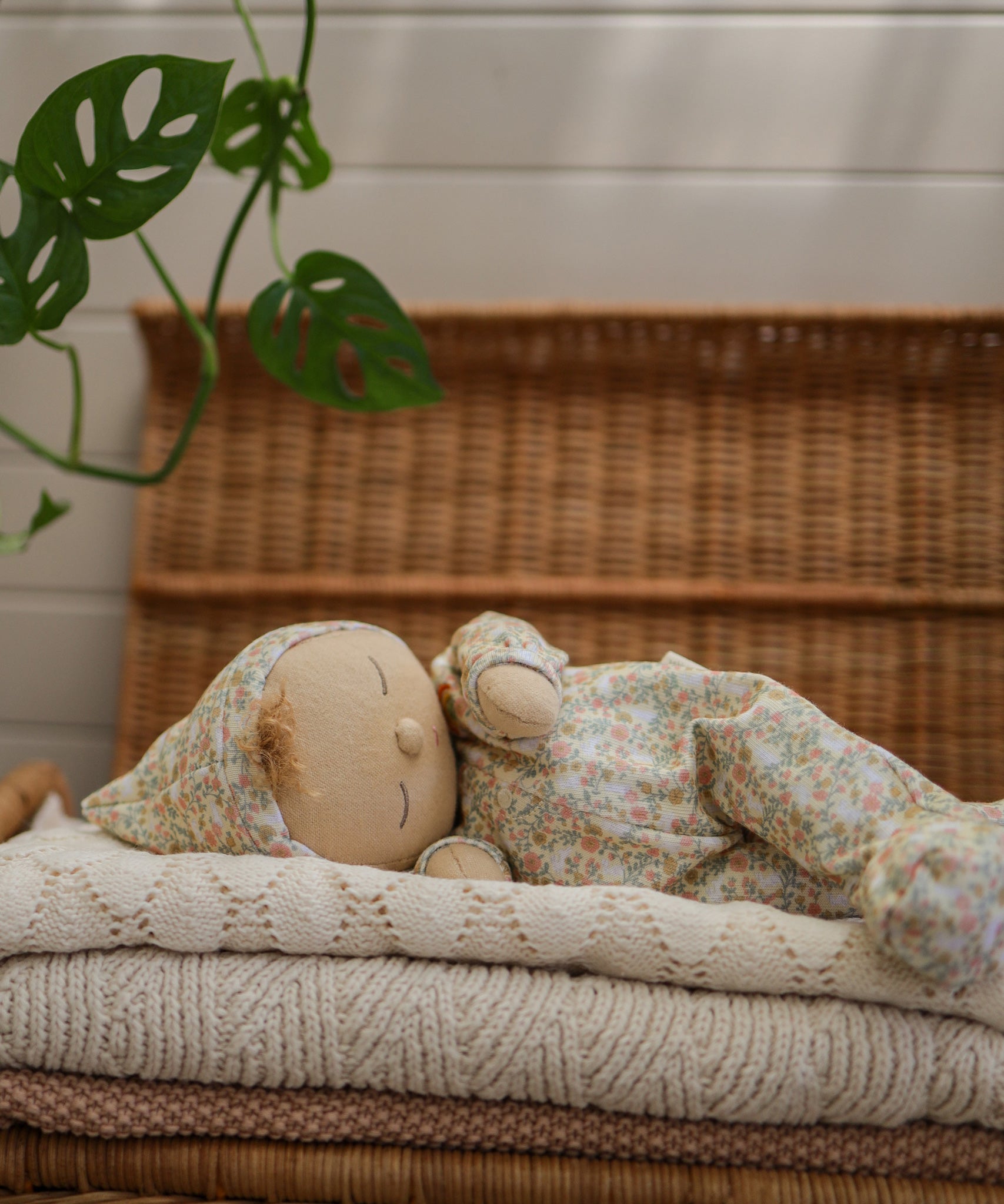 A side on view of an Olli Ella Dozy Dinkum Doll Custard laying on a pile of blankets.