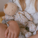 A close up of a Olli Ella Dozy Dinkum Doll Custard in a child's arm. 