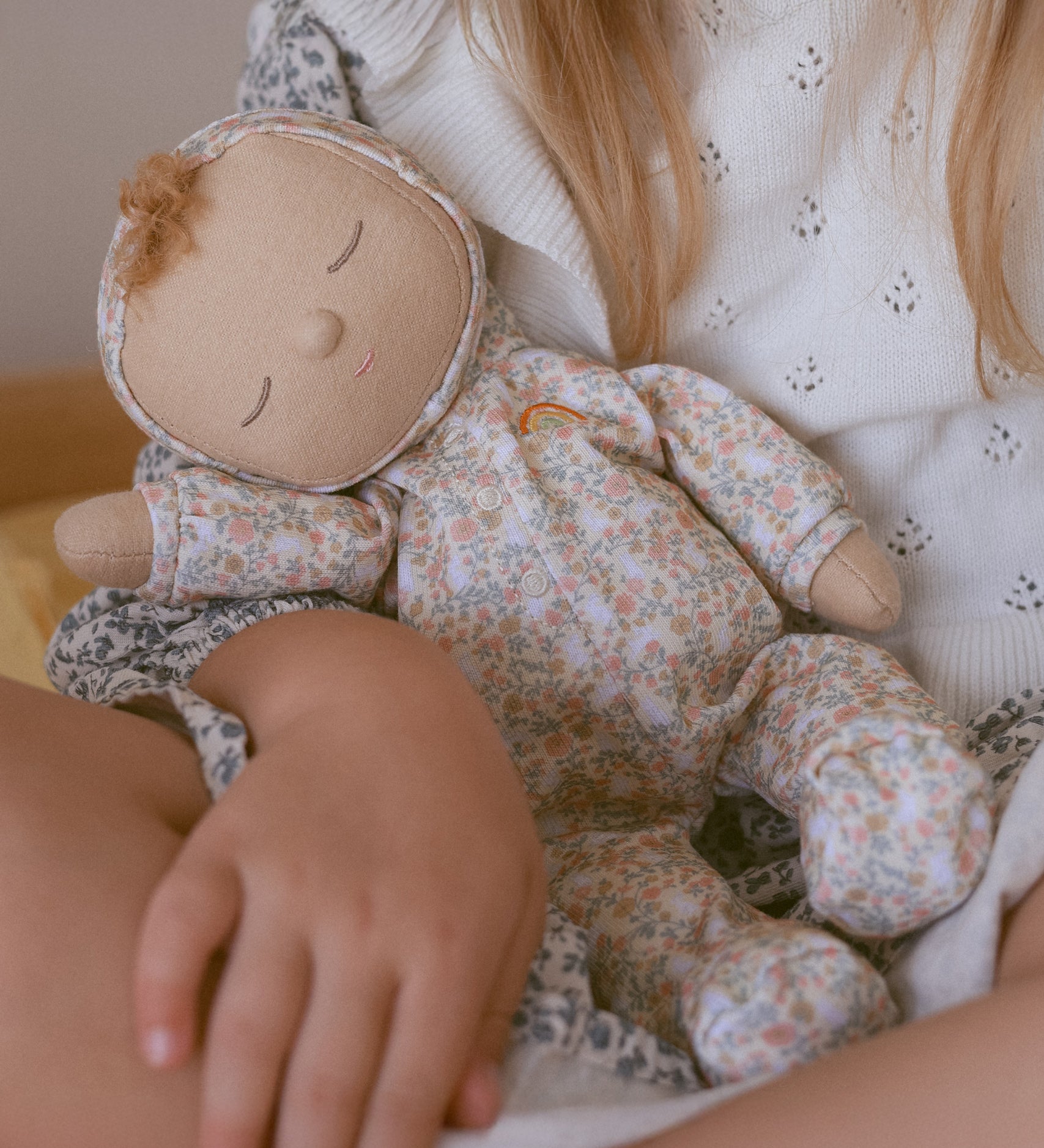 A close up of a Olli Ella Dozy Dinkum Doll Custard in a child's arm. 