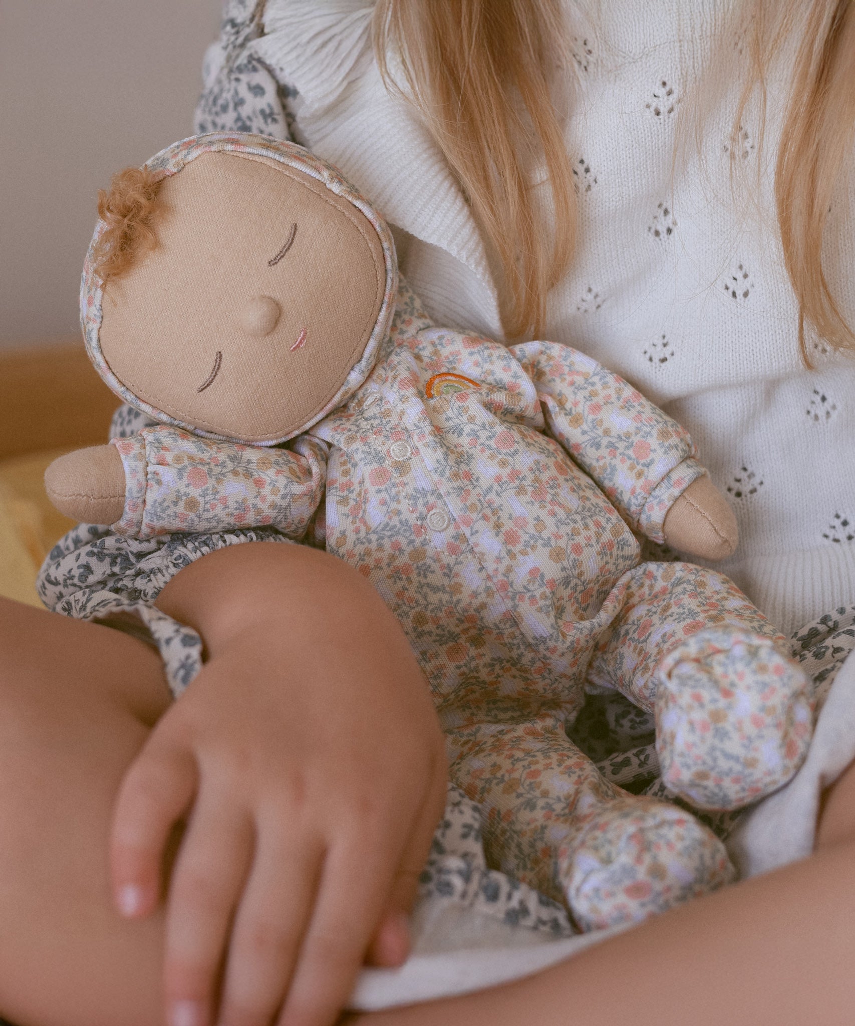 A close up of a Olli Ella Dozy Dinkum Doll Custard in a child's arm. 