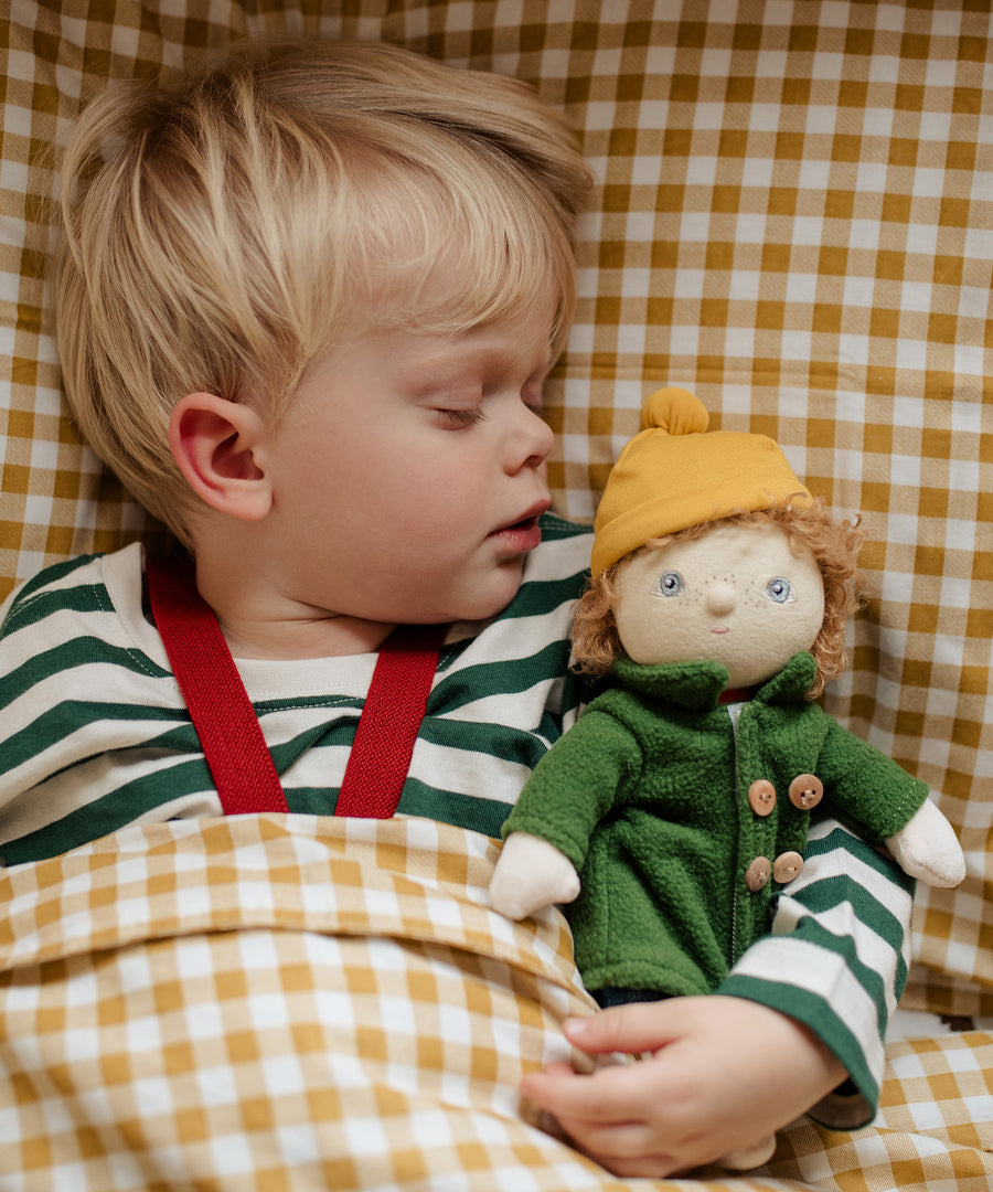 Toddler asleep next to Charlie Chestnut a Dress Me Dinky Doll by Olli Ella, with yellow gingham bedding.