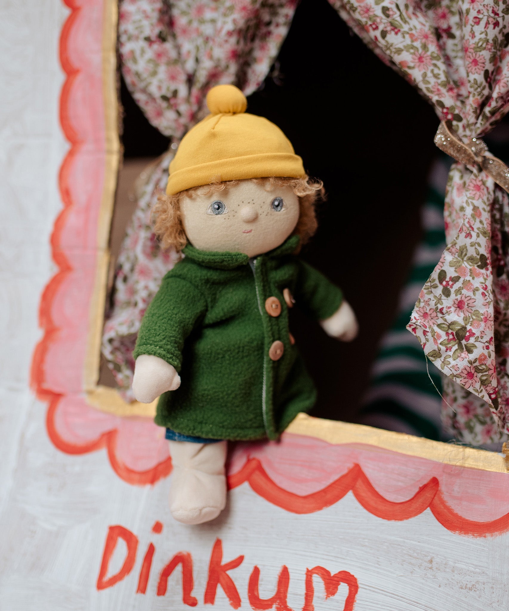 Charlie Chestnut is a Dress Me Dinky Doll by Olli Ella, complete with a removable cosy green fleece trench coat, yellow bobble beanie hat . At a child's puppet theatre.