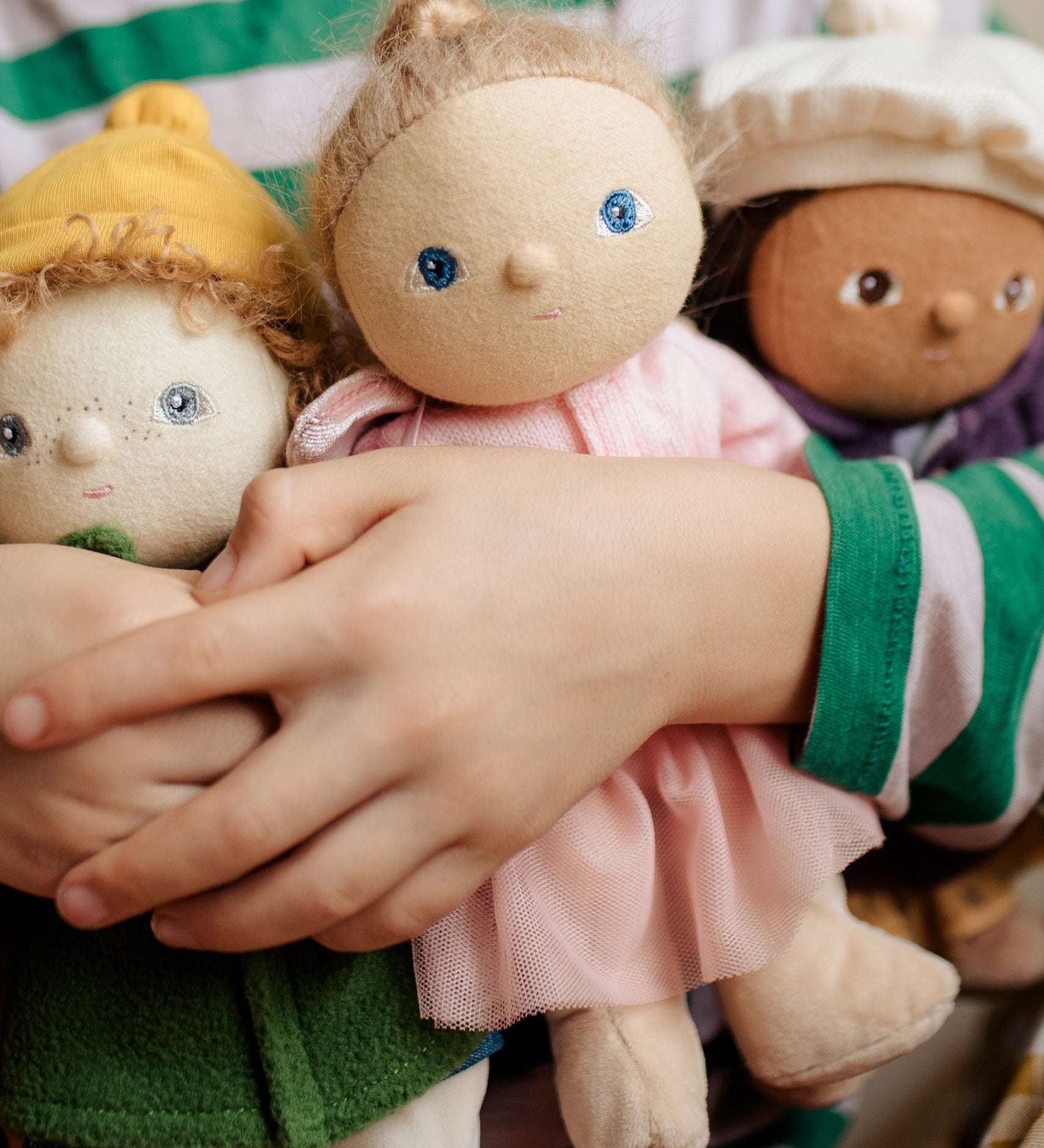 Three Dress Me Dinky dolls being held by a child in a green and white stripe top. 