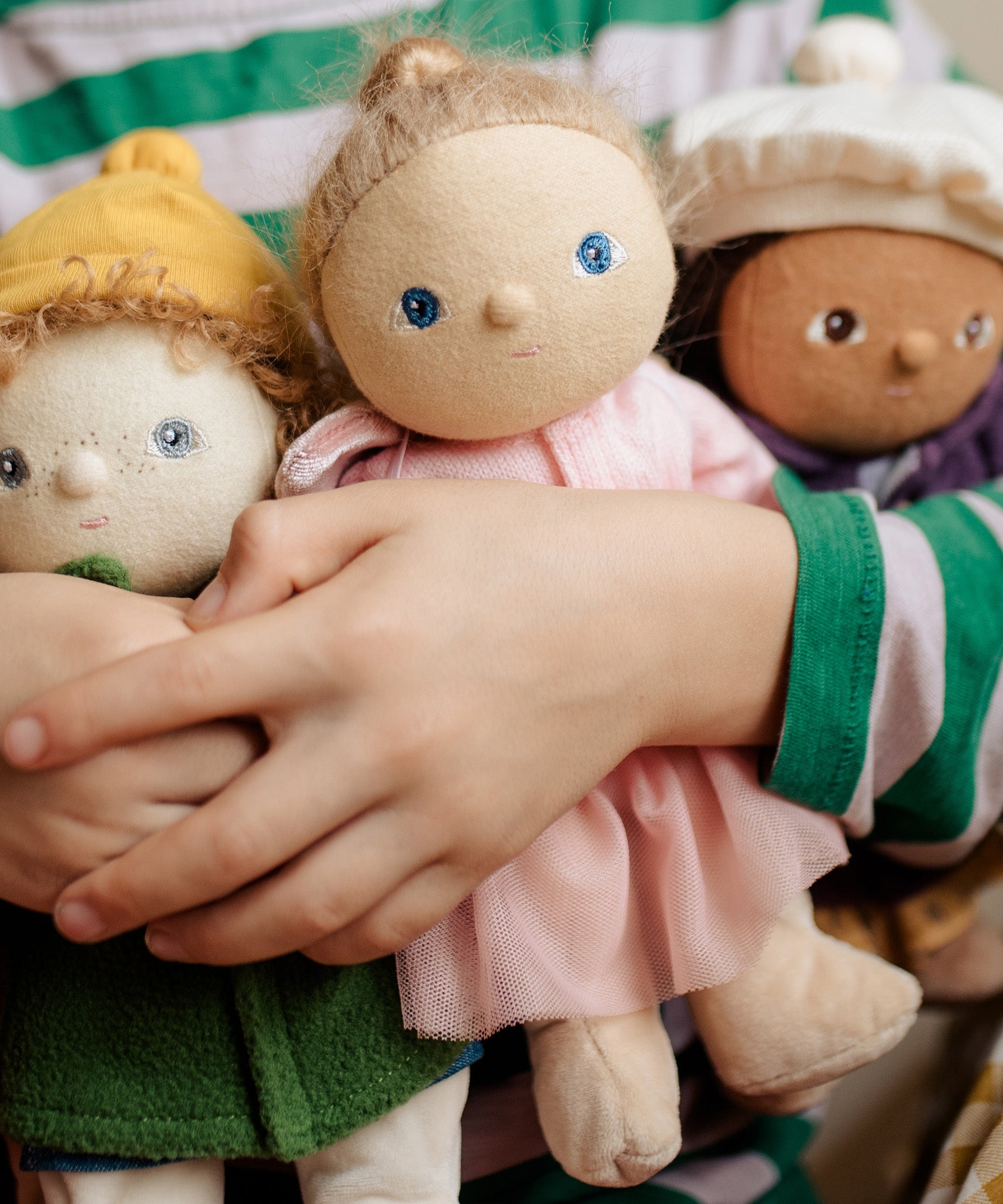 Three Dress Me Dinky dolls being held by a child in a green and white stripe top. 