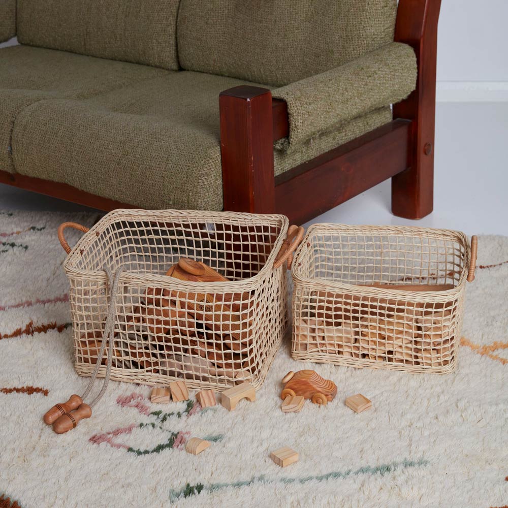 2 natural woven olli ella cabouche rattan baskets filled with wooden toys on a white carpet next to a green