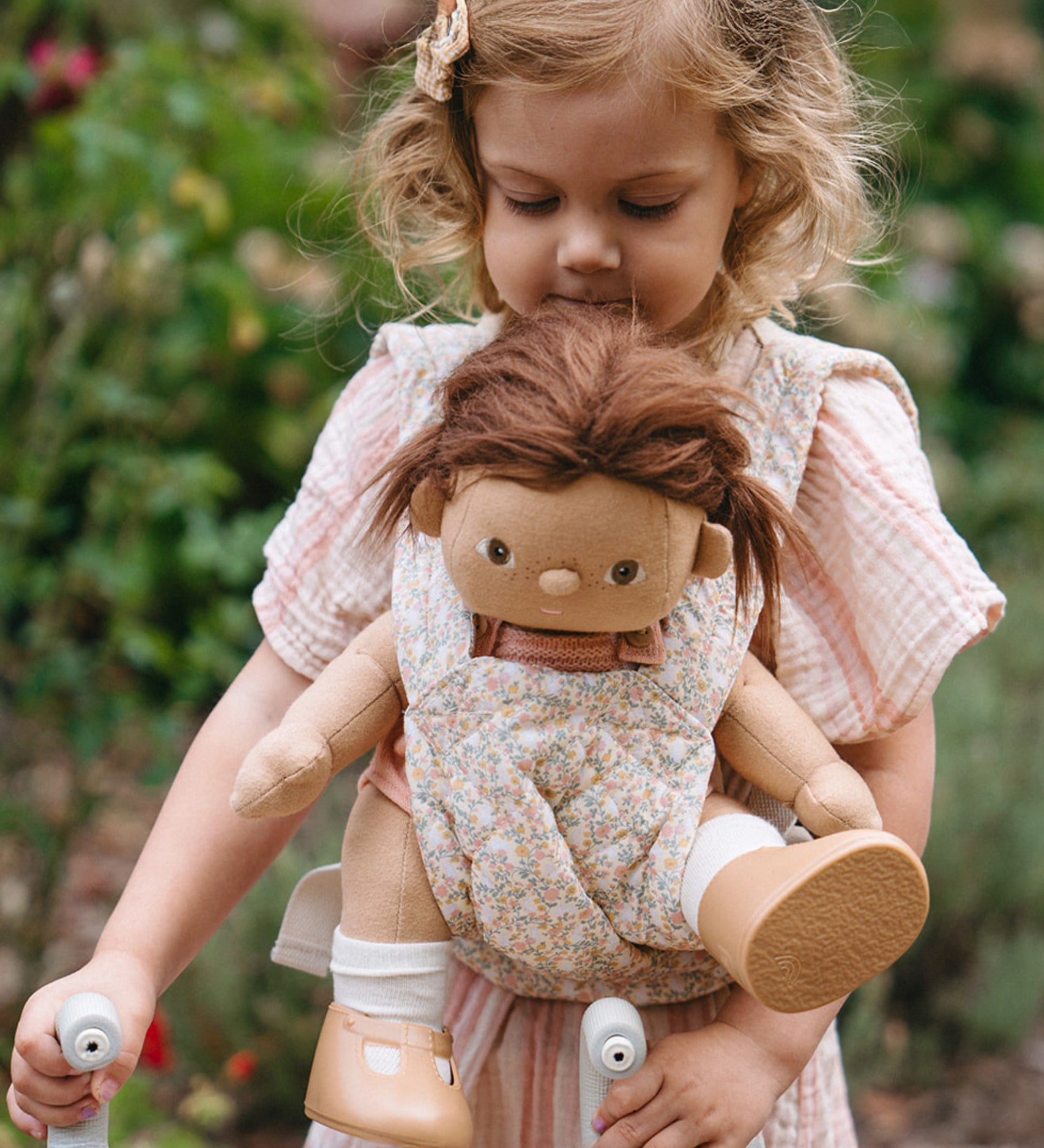 A child carrying a Dinkum doll using the Olli Ella Garden Floral Gardenia print Dinkum Dolls Quilted Toy Carrier.