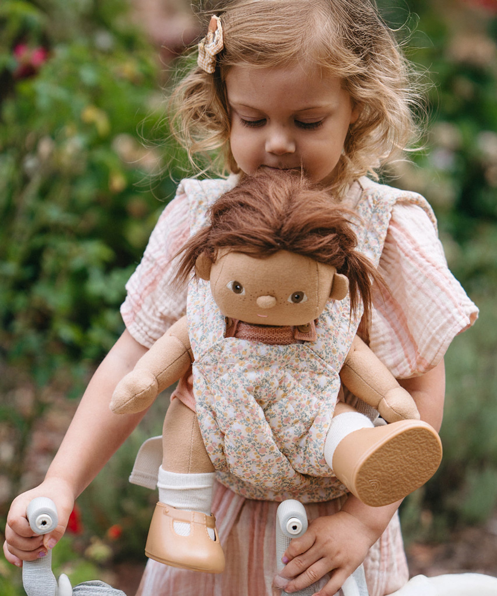 A child carrying a Dinkum doll using the Olli Ella Garden Floral Gardenia print Dinkum Dolls Quilted Toy Carrier.