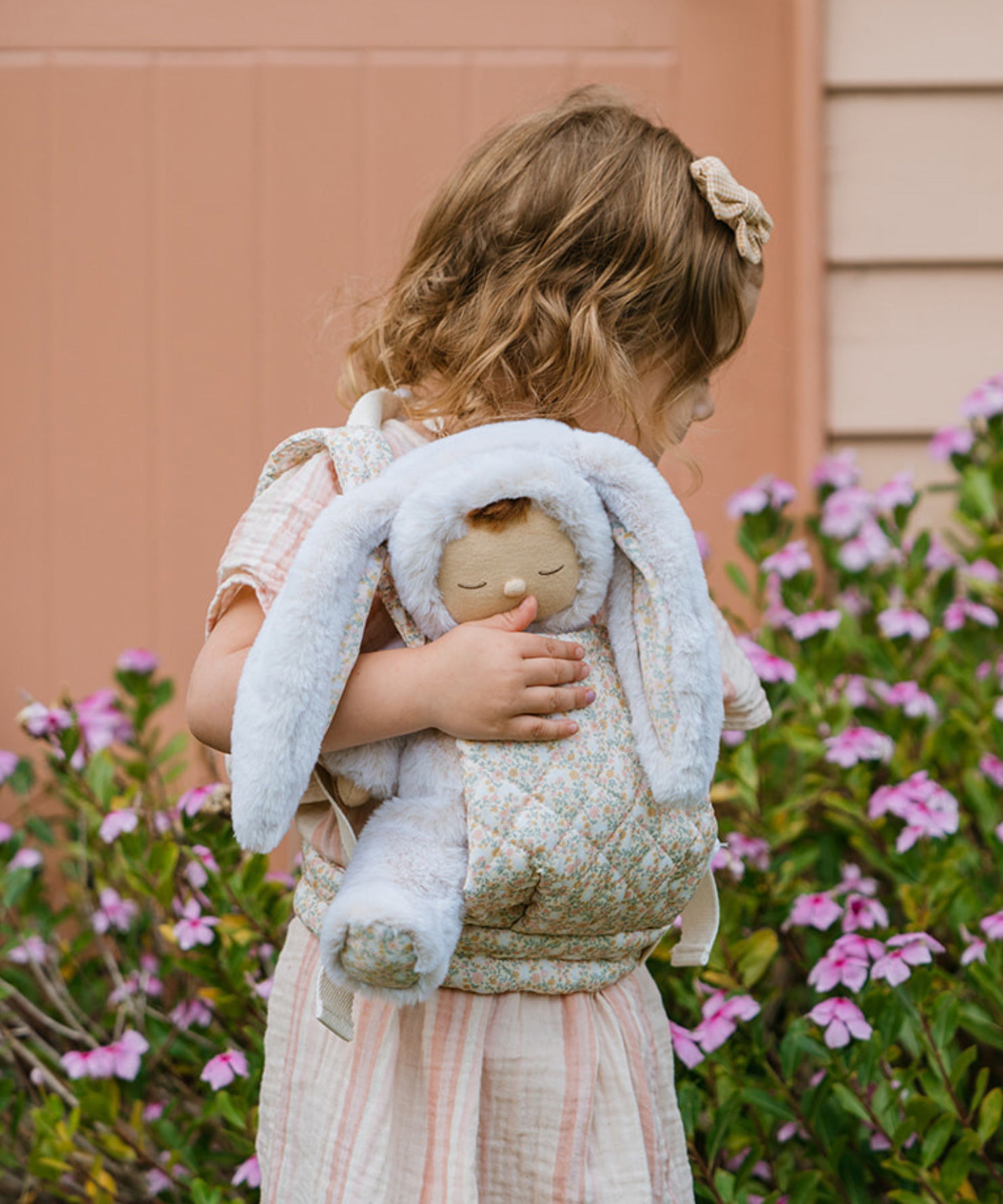 A child carrying a Dozy Dinkum Bunny doll using the Olli Ella Garden Floral Gardenia print Dinkum Dolls Quilted Toy Carrier.