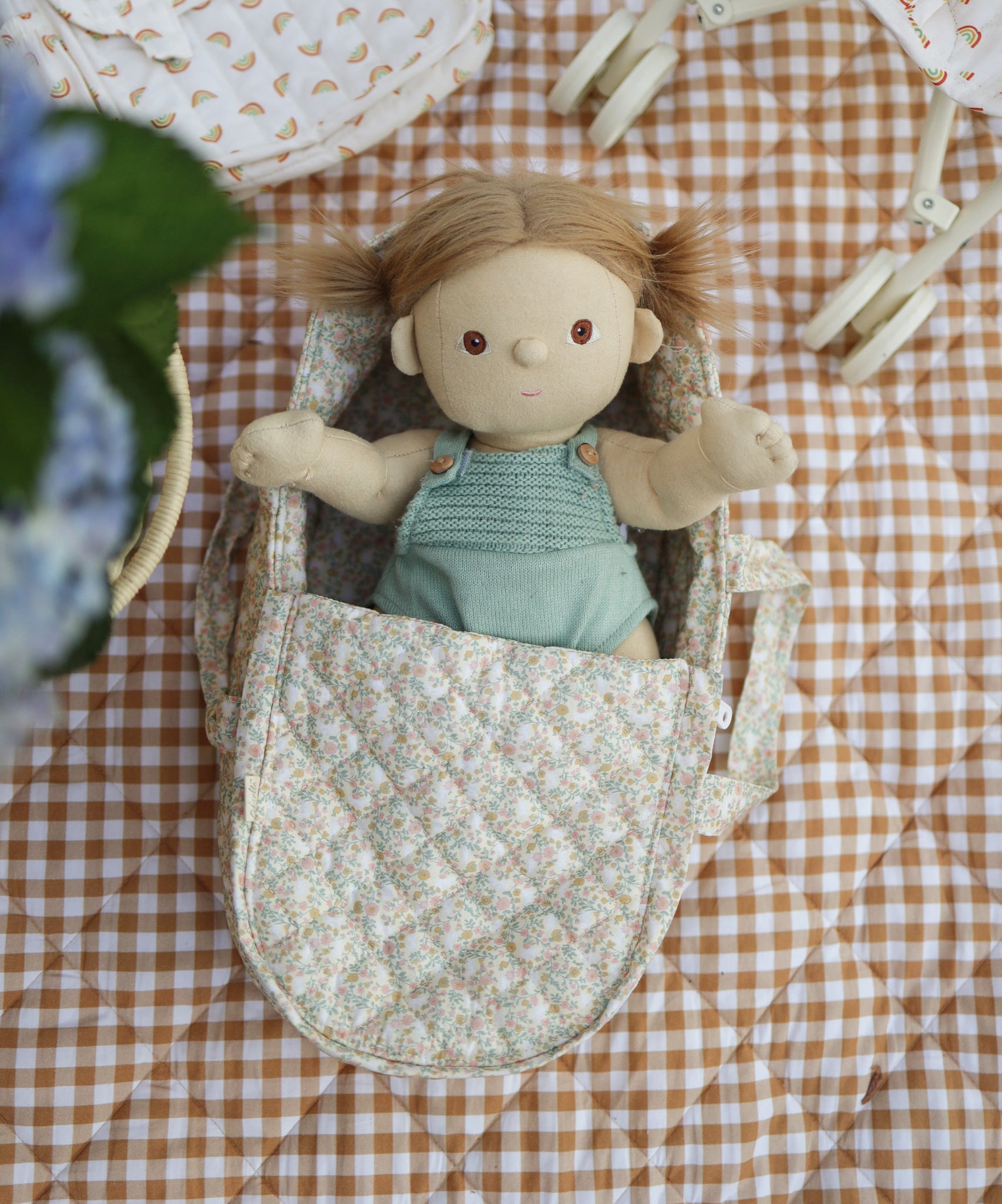 A Dinkum Doll laying in the Olli Ella Garden Floral Gardenia print Dinkum Dolls Quilted Carry Cot 