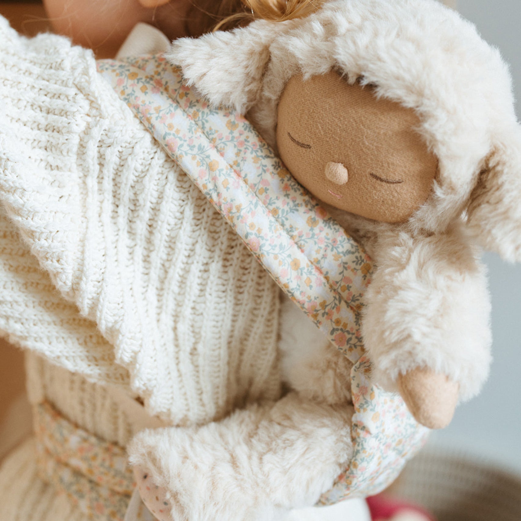 A close up of a child carrying a Dozy Dinkum doll using the Olli Ella Garden Floral Gardenia print Dinkum Dolls Quilted Toy Carrier.