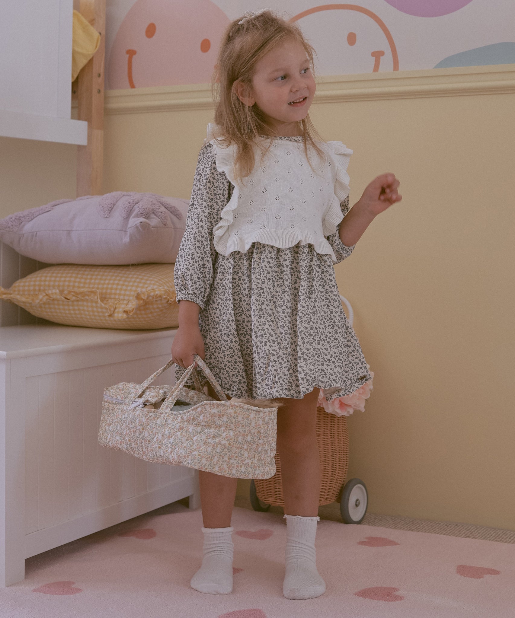 A child holding the Olli Ella Garden Floral Gardenia print Dinkum Dolls Quilted Carry Cot in their hand by the straps. 