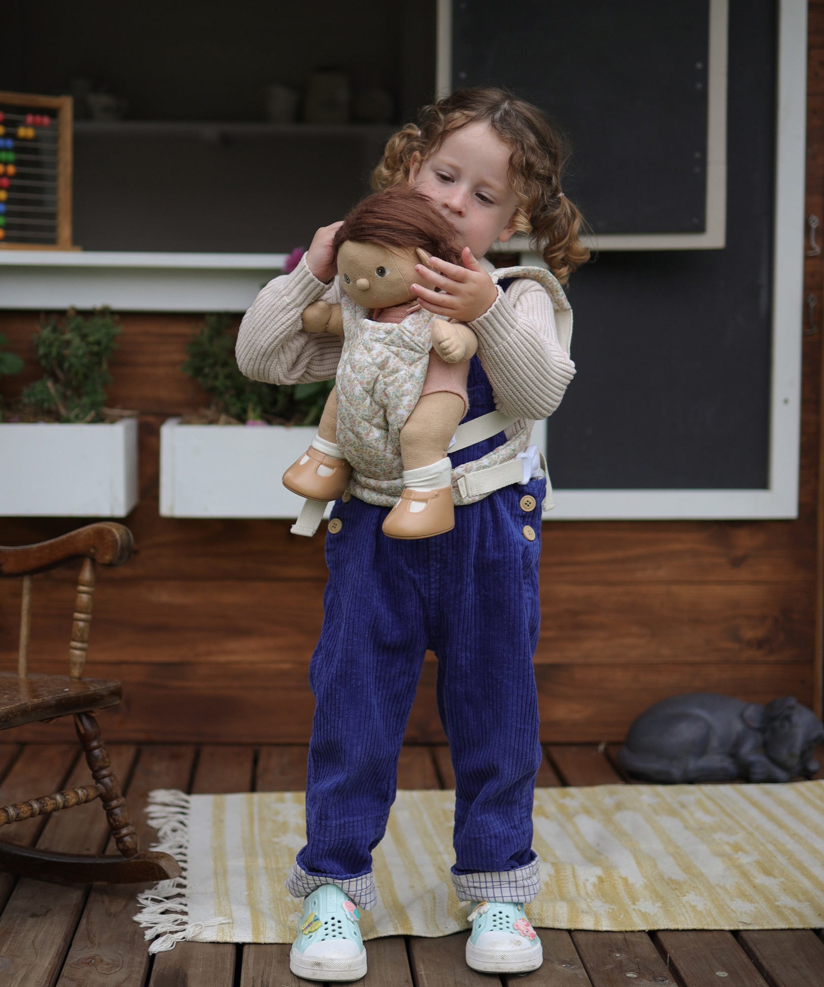 A child carrying a Dinkum doll using the Olli Ella Garden Floral Gardenia print Dinkum Dolls Quilted Toy Carrier.