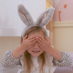 A child wearing the grey Olli Ella Fluffle Bunny Ear Headband, they have their hands covering their eyes. 