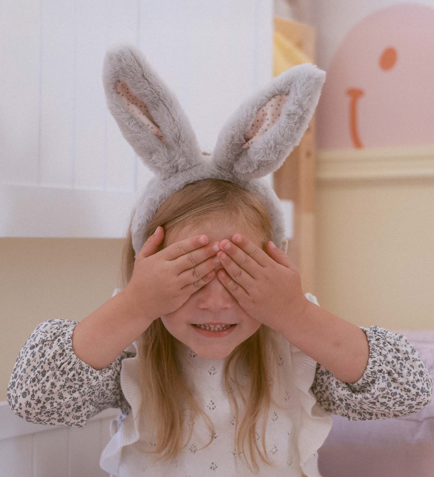 A child wearing the grey Olli Ella Fluffle Bunny Ear Headband, they have their hands covering their eyes. 