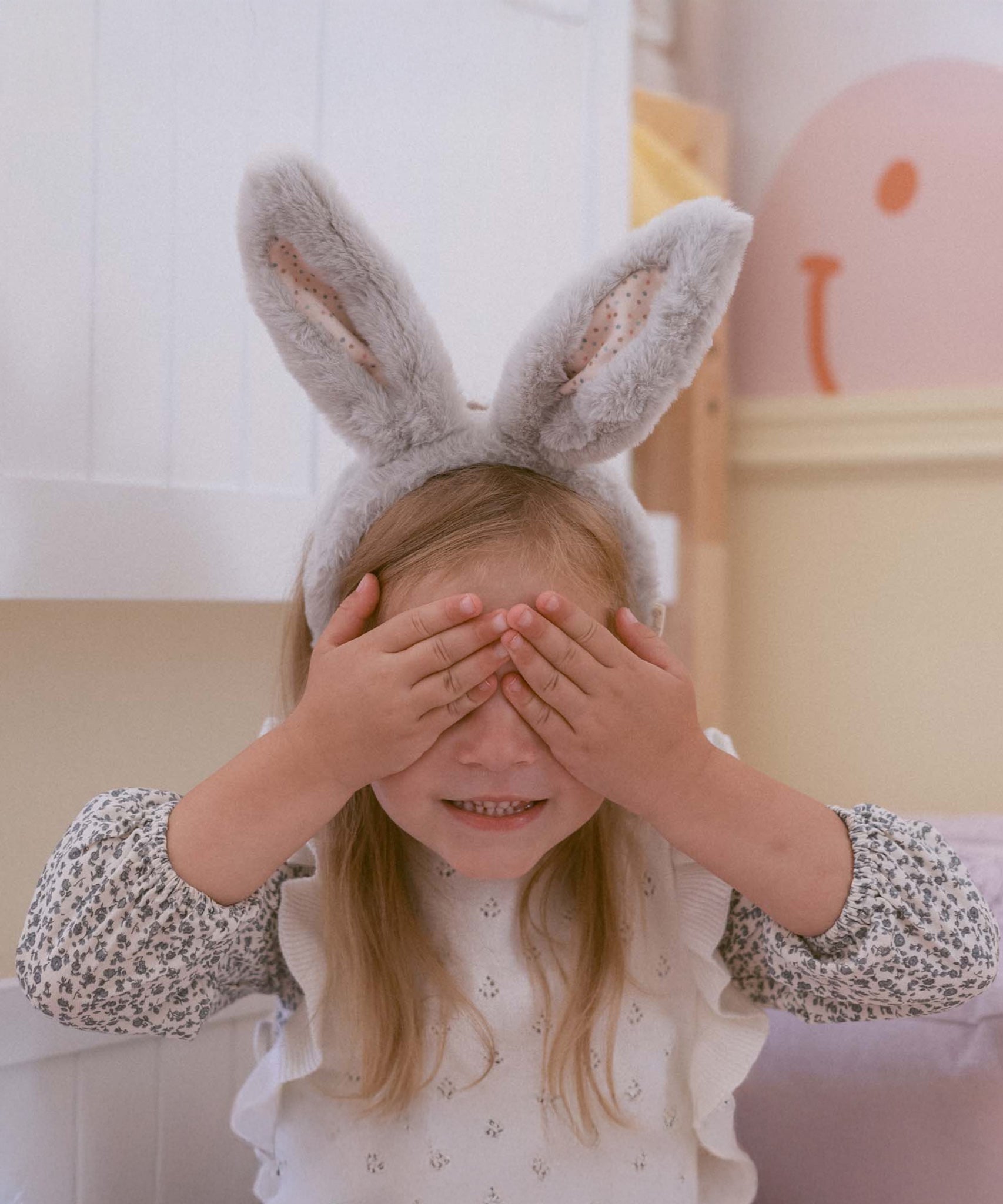 A child wearing the grey Olli Ella Fluffle Bunny Ear Headband, they have their hands covering their eyes. 