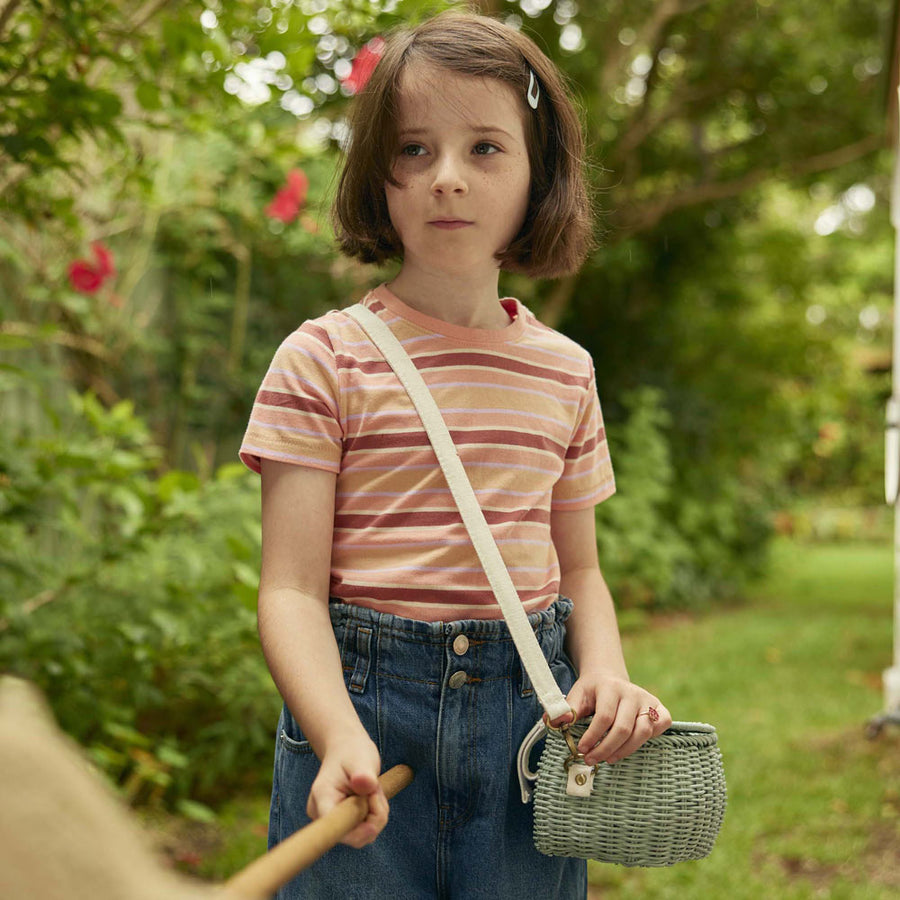 Close up of a girl stood in a garden wearing the olli ella mini chari rattan bag in blue