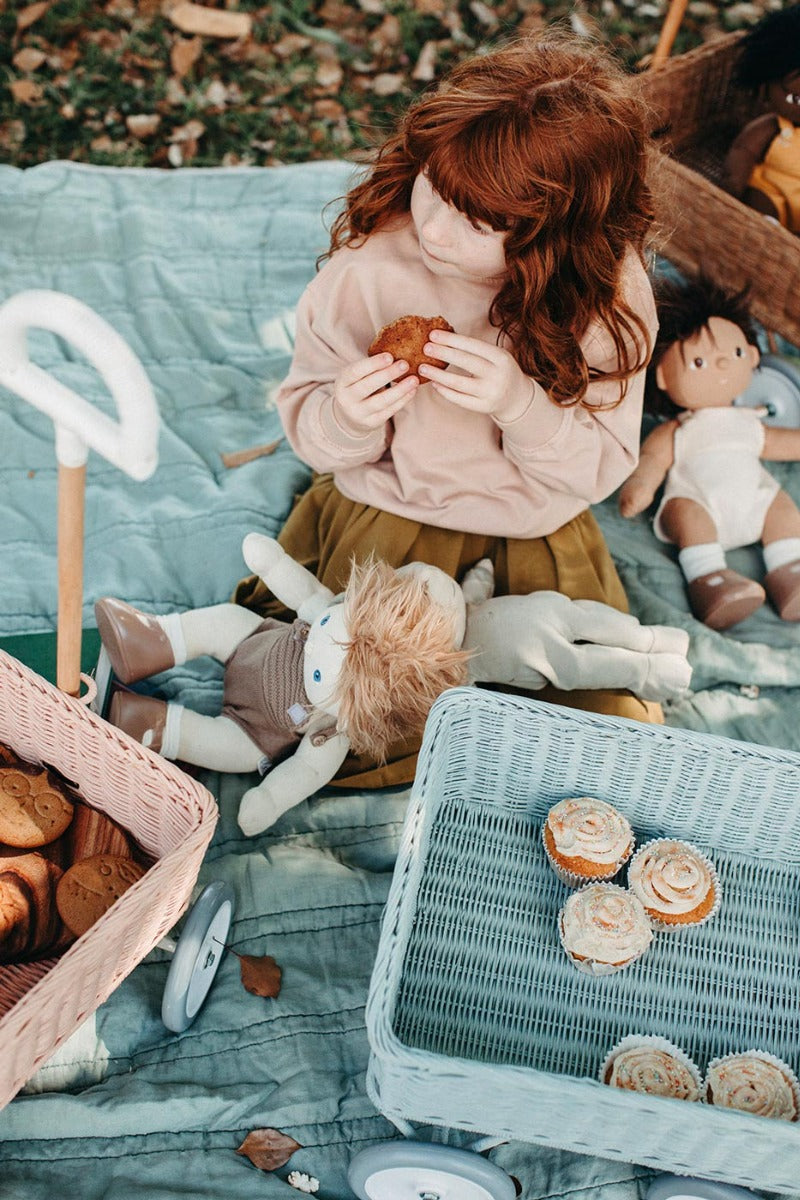 Girl sat down on a blue blanket eating a cake next to the Olli Ella vintage blue wonder wagon