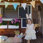 A child wearing the pink Olli Ella Fluffle Bunny Ear Headband. The child is dressed in a cream coloured dress pulling along an olli ella dinkum doll in a luggy style basket. 