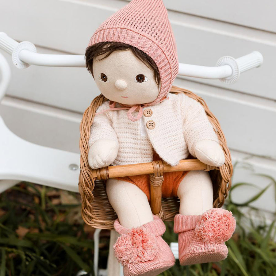 Olli Ella dinkum doll sat in a wooden basket seat wearing the pink bloom knitted accessory set