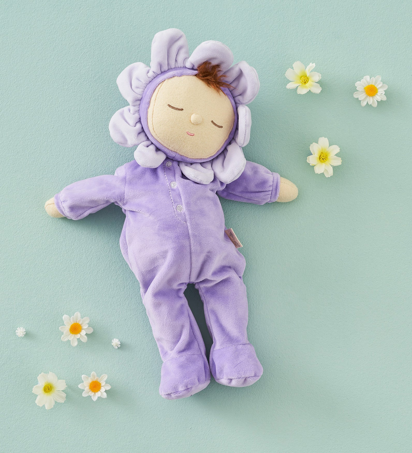 Olli Ella Lavender Pickle Dozy Dinkum Doll laying on a green surface surrounded by little white flower heads. 