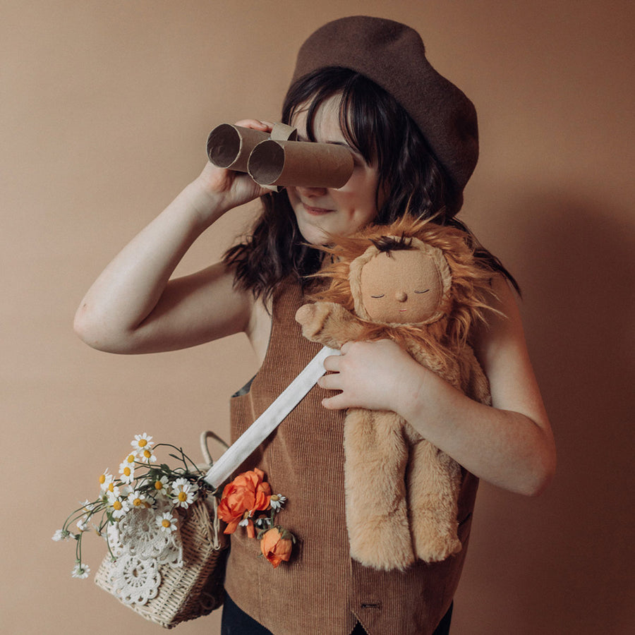 Child holding the Olli Ella Lion Pip Cozy Dinkum Doll in one hand whilst holding onto a homemade cardboard tube binoculars in the other