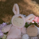 The Olli Ella Pink Bunny Moppet Lullaby Cozy Dinkum placed on a bunch of flowers with another dozy dinkum besides it. 