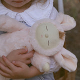 A close up of the Olli Ella Pink Bunny Moppet Lullaby Cozy Dinkum in a child's arms.