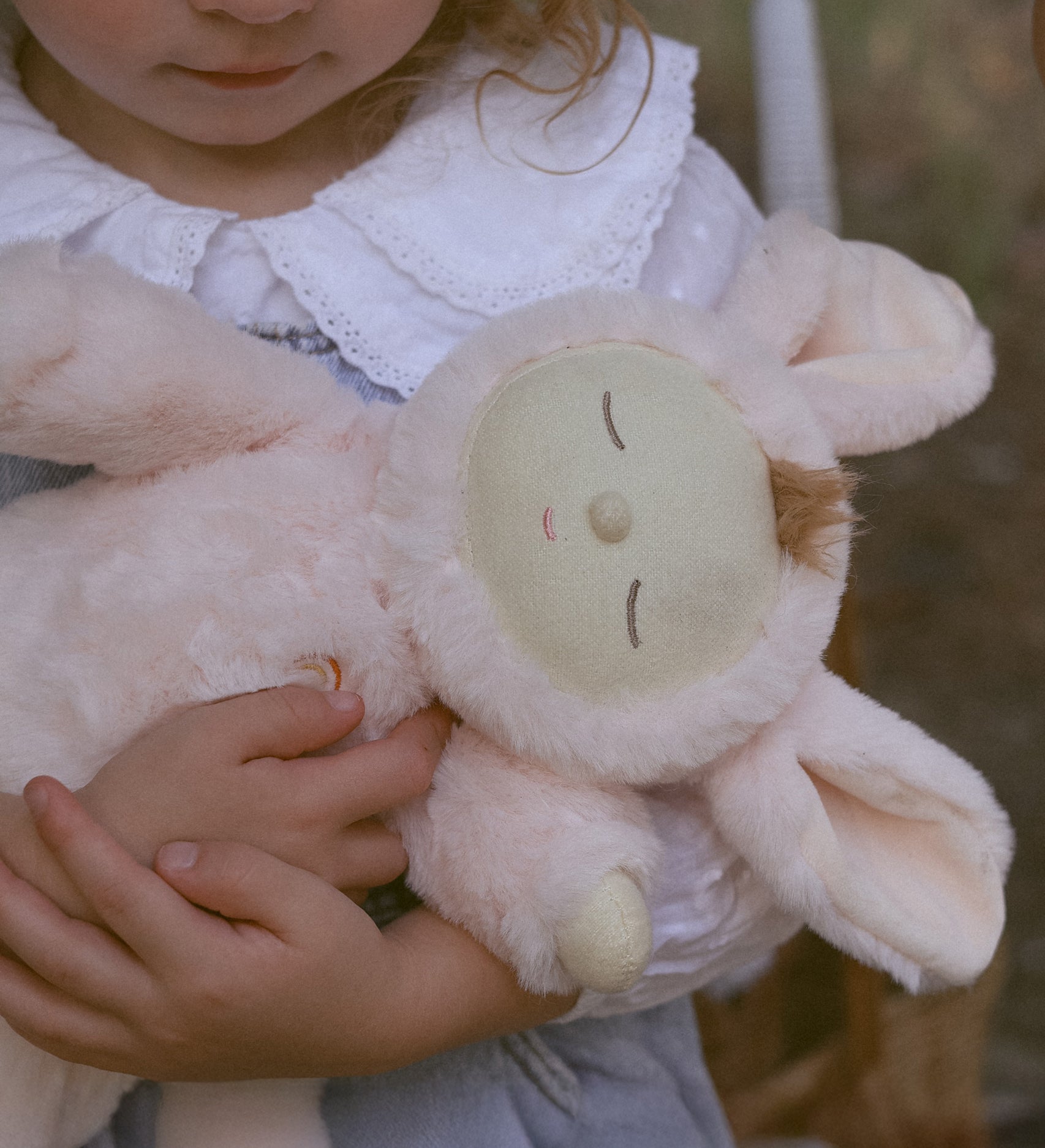 A close up of the Olli Ella Pink Bunny Moppet Lullaby Cozy Dinkum in a child's arms.