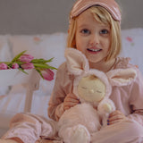 A child in pink pyjamas holding the the Olli Ella Pink Bunny Moppet Lullaby Cozy Dinkum. 