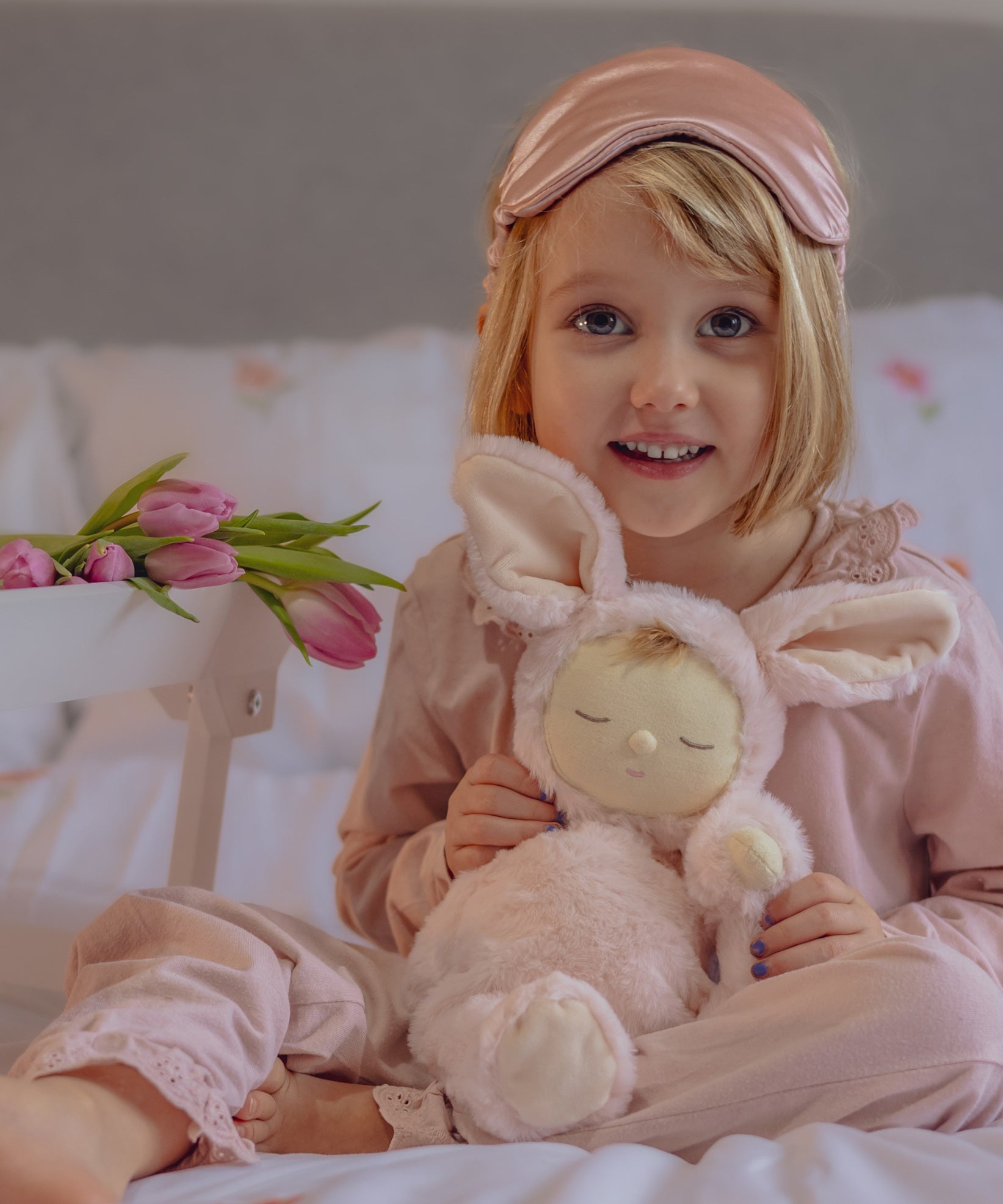 A child in pink pyjamas holding the the Olli Ella Pink Bunny Moppet Lullaby Cozy Dinkum. 