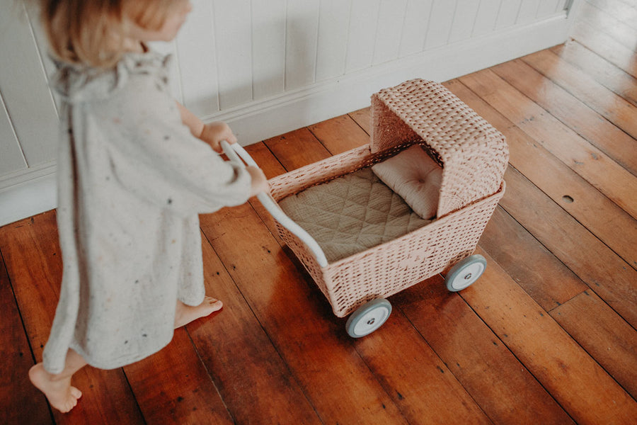 Girl pushing an olli ella natural rattan strolley with the seafoam bedding on a wooden floor