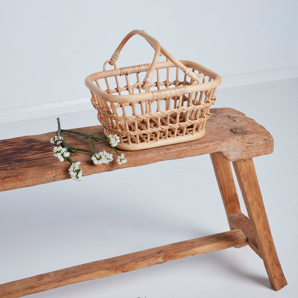 Olli ella eco-friendly woven rattan tarry basket in the wheat colour next to some white flowers on a wooden bench