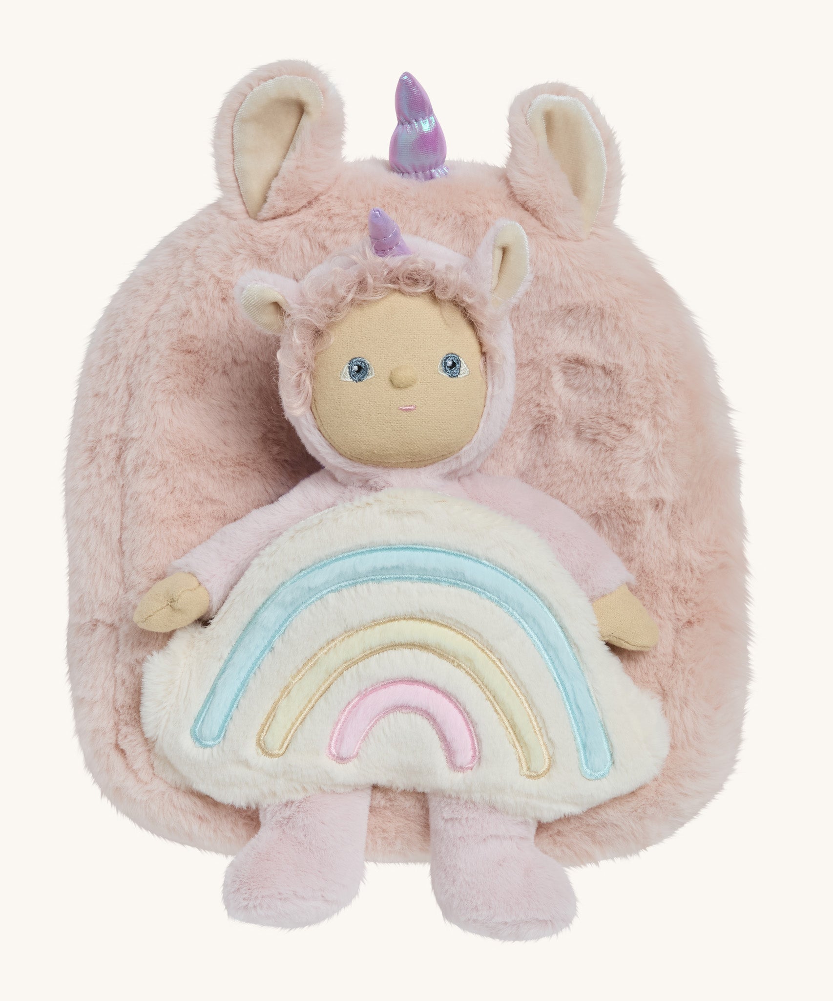 A OIli Ella pink fluffy unicorn backpack with a rainbow on the front  with a dinky dinkum doll sitting on the bag on a cream background.