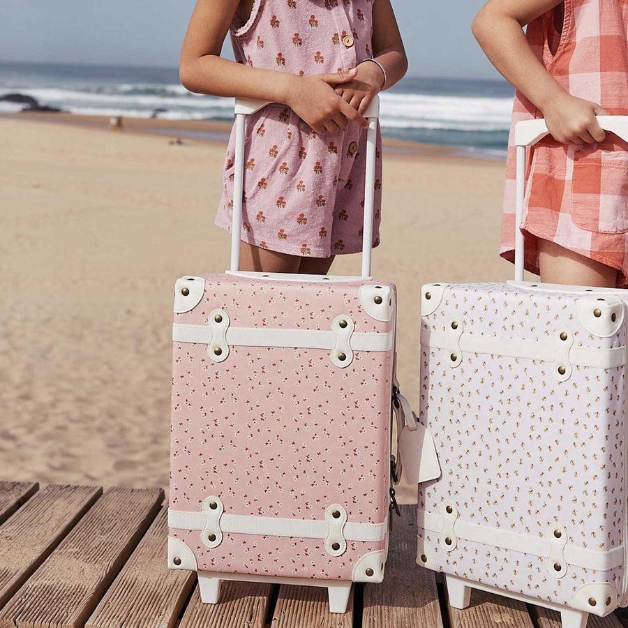 Child sitting on decking with an Olli Ella Pink Daisies See-Ya Suitcase  on it's side next to them