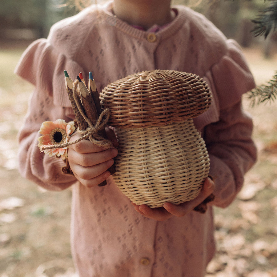 A close up of a child holding an Olli Ella Porcini basket and wooden twig pencils in their hands