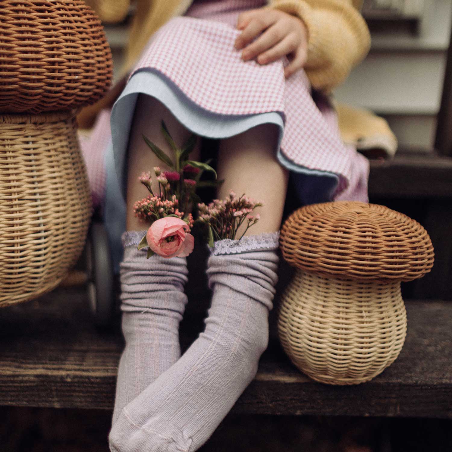 A close up of a child sitting down with an Olli Ella Porcini mushroom shaped basket next to them