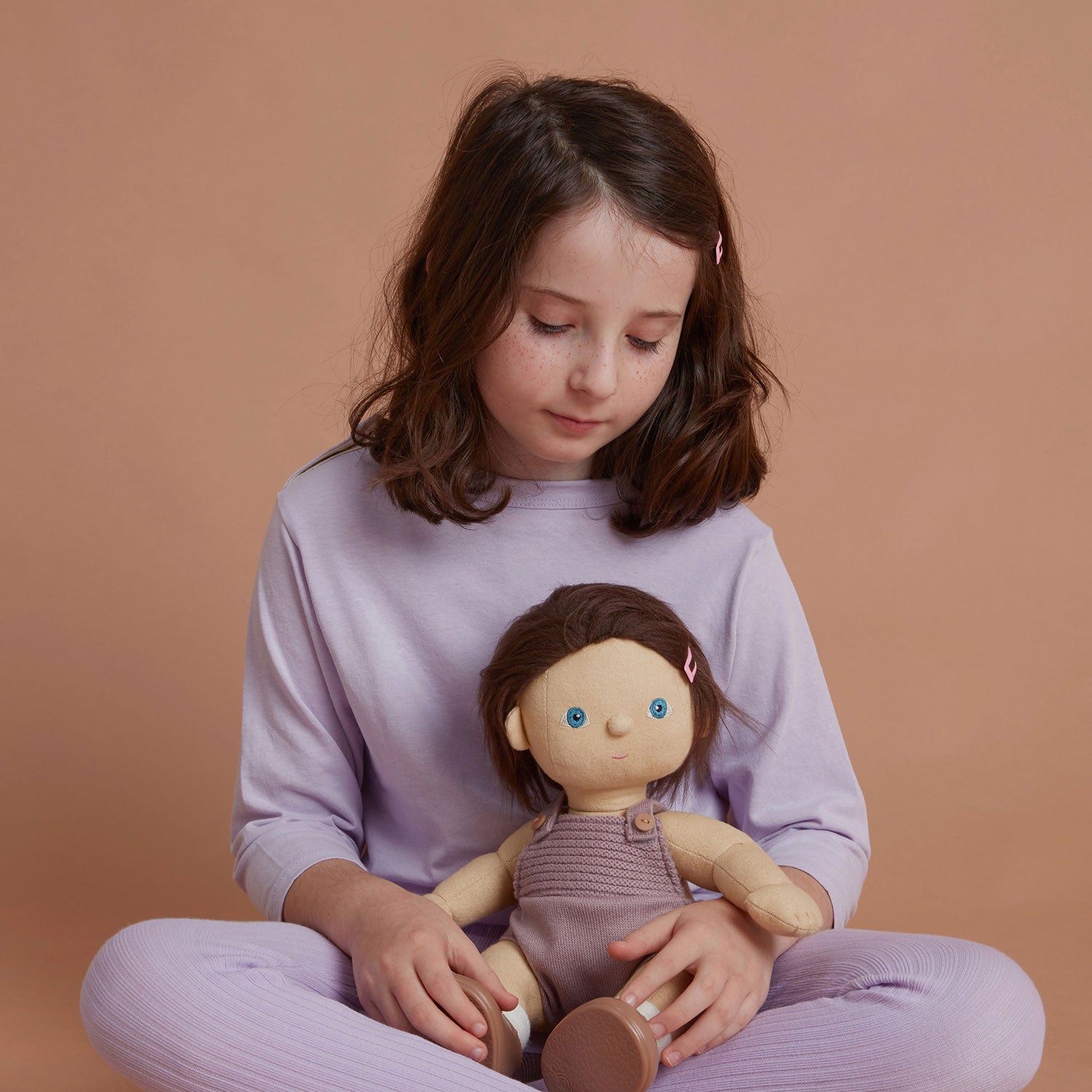 soft bodied Dinkum Doll with hair tied up in little bunches at the side of their head sitting down pictured on a plain coloured background