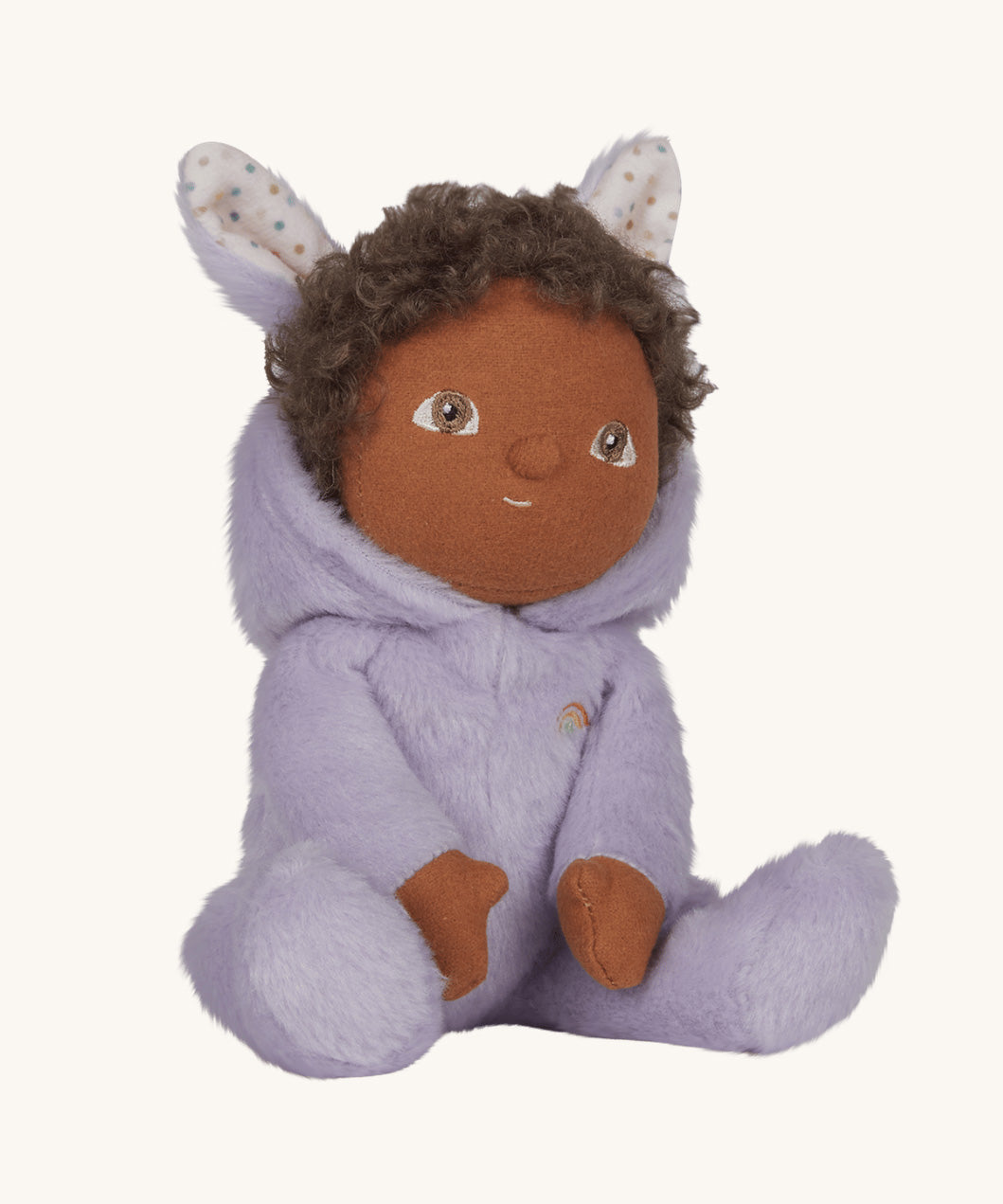 Olli Ella purple coloured Babs Bunny Dinky Dinkum Doll in a seated position. The bunny ear hood is pulled down showing the curly dark coloured hair