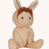 Olli Ella light sand coloured Bubba Bunny Dinky Dinkum Doll in a seated position. The dolly's red coloured curly hair can be seen peeping out from underneath the bunny eared hood. 