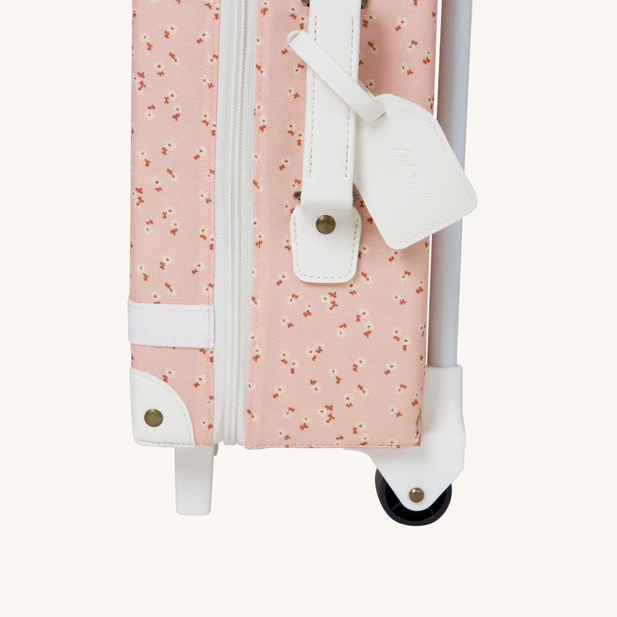 Close up of the tag on the Olli Ella See-Ya Suitcase with a Pink Daisies print pictured on a plain background