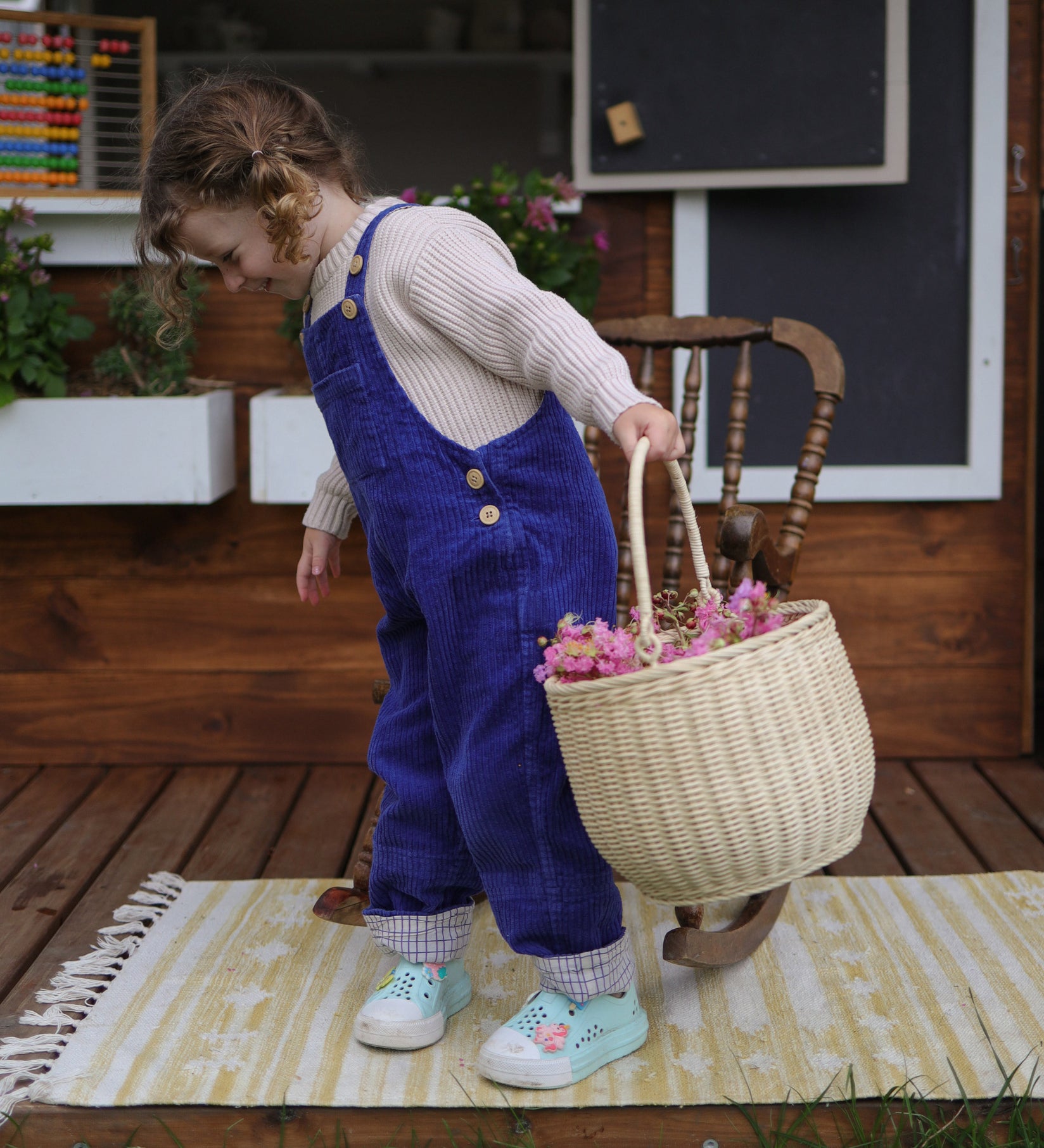 A child holding an Olli Ella Large Strw Rattan Gathering basket in their hand filled with flowers.