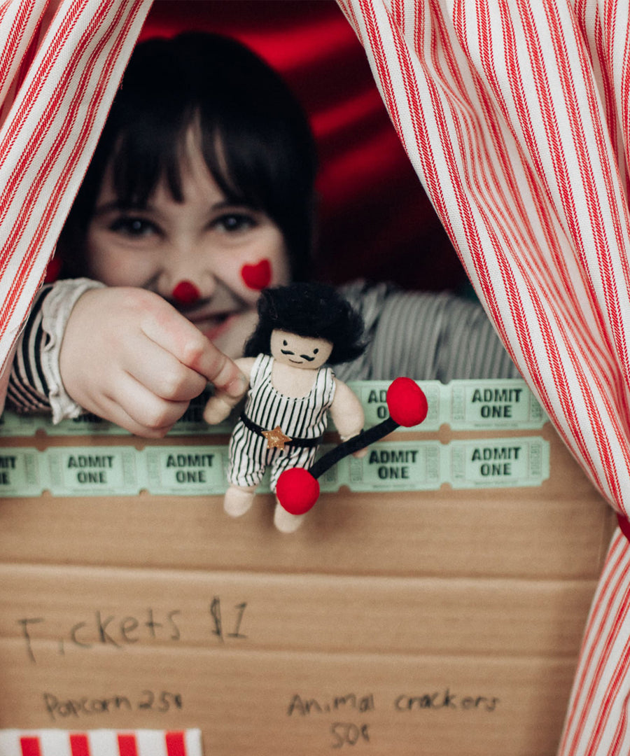 A child holding Olli Ella Holdie Circus Folk Samson The Strongman at a ticket booth stand