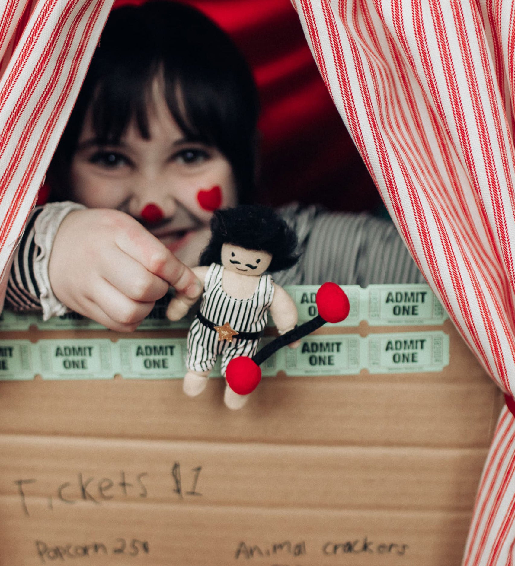 A child holding Olli Ella Holdie Circus Folk Samson The Strongman at a ticket booth stand