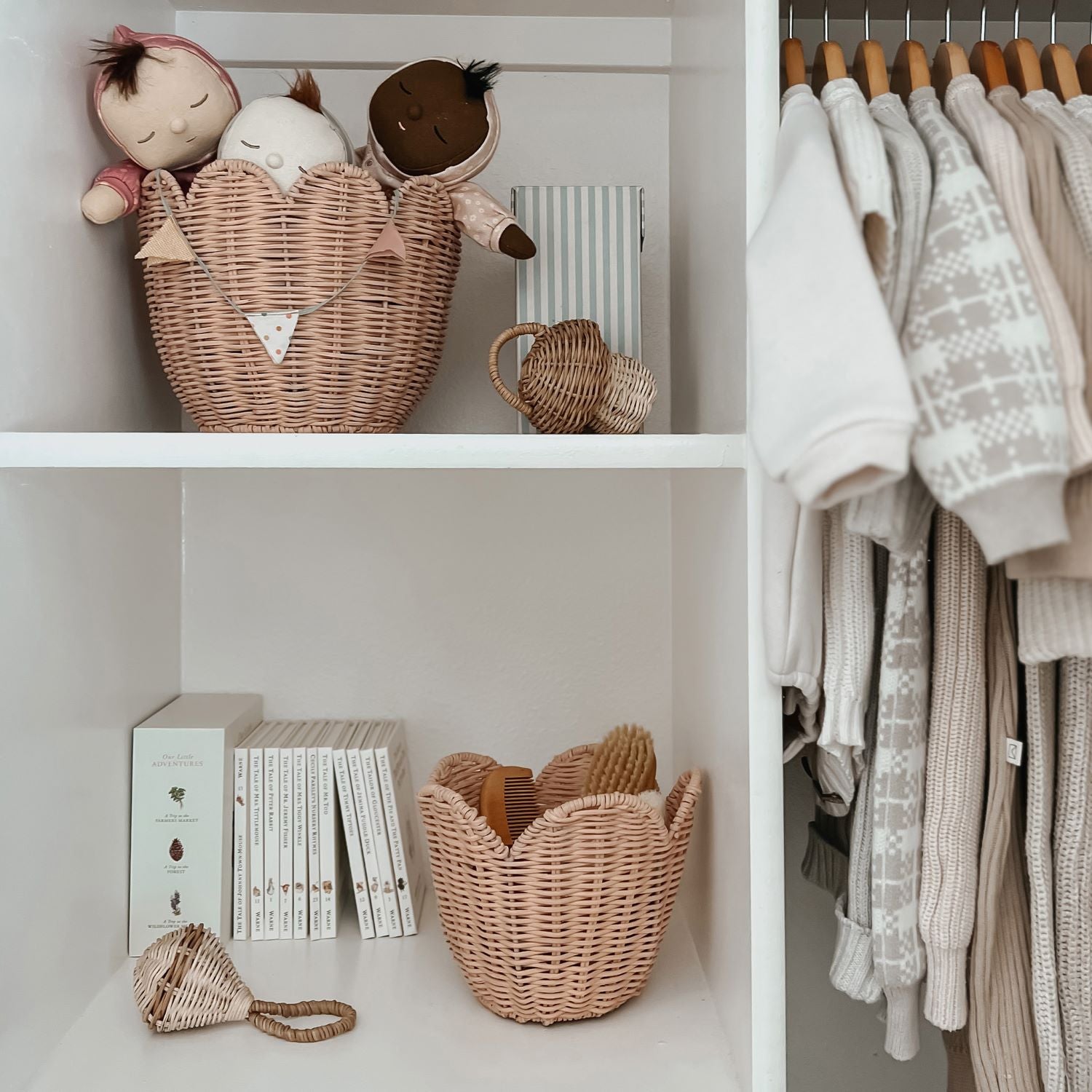 The Olli Ella Rattan Lily Basket Set in Seashell Pink on shelves in a wardrobe. The larger basket is holding Dozy Dinkum dolls on the top shelf