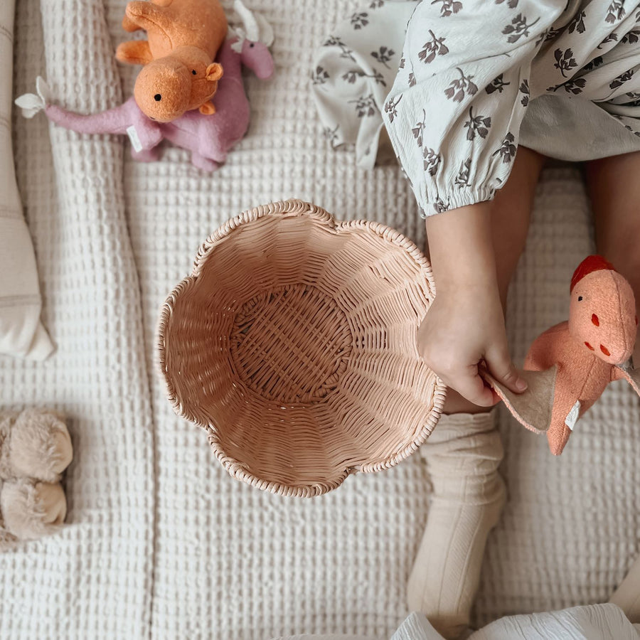 A child is sat on the bed with the Olli Ella Rattan Lily Basket Set in Seashell Pink taking out soft toys.