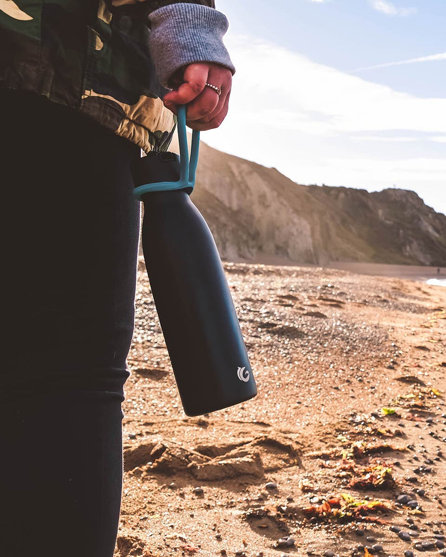 Close up of hand holding a One Green Bottle life collection canteen on a sunny beach 