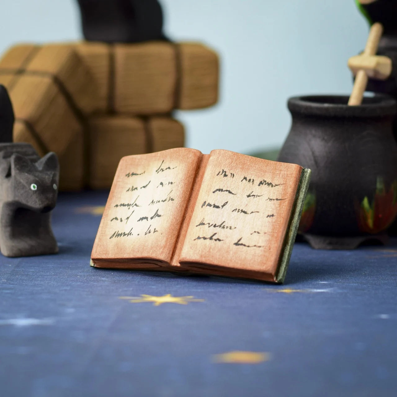 I put a spell on you, with the Bumbu Toys Open Spell Book! This image shows the Book stood in front of a witch brewing a potion in a coldron, with the Bumbu Scardy cat looking on