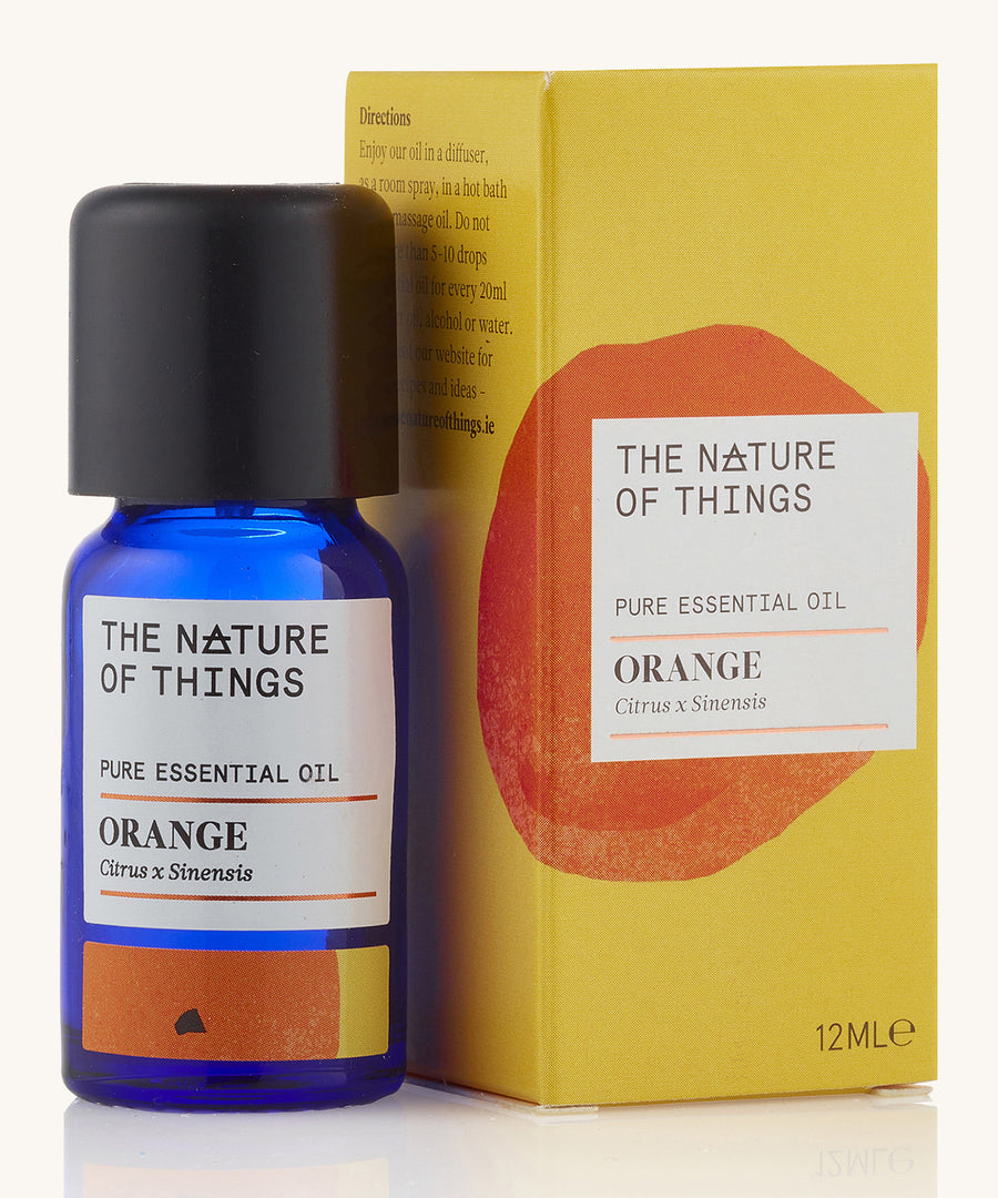 Orange pure essential oil in a blue glass bottle in front of a decorative yellow cardboard box.