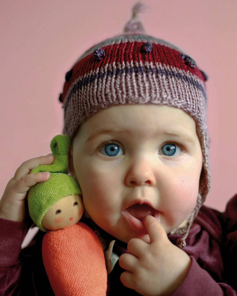 baby holding an organic carrot shaped soft toy which has a face and a green hat