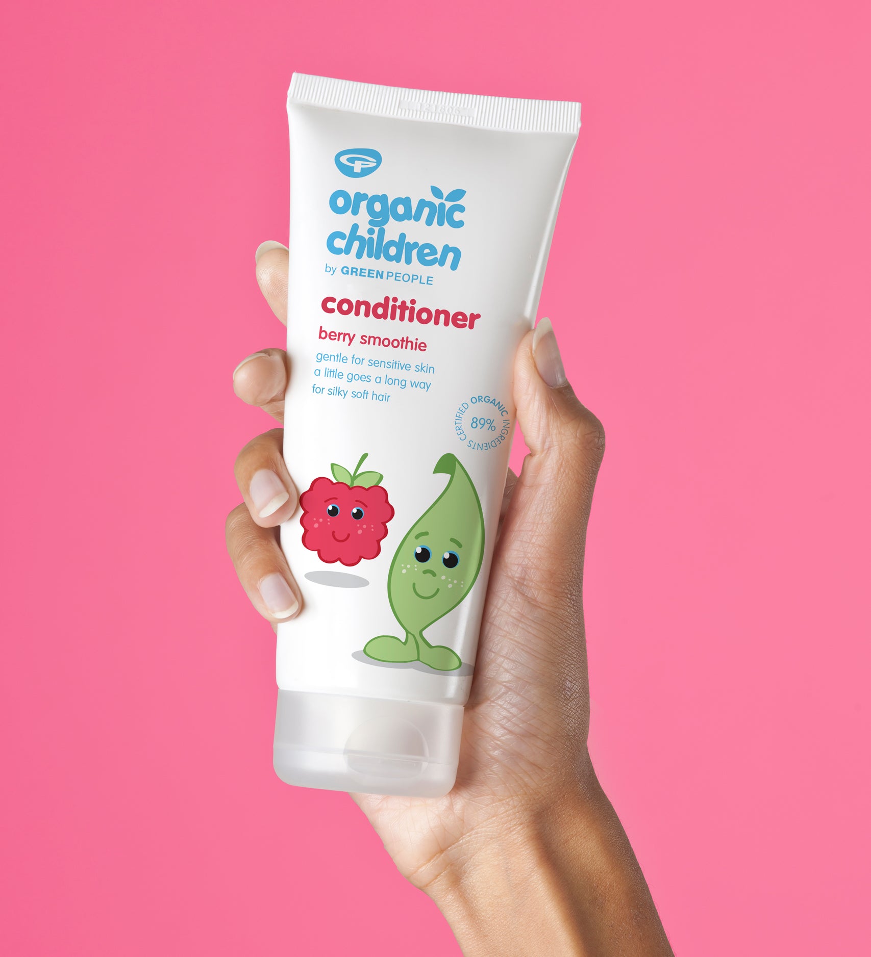 Organic Children Berry Smoothie Conditioner in an adult's hand pictured against a bright pink background. 